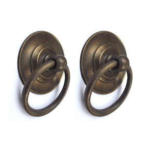 May include: Two antique brass ring pulls with a circular base and a ring handle. The pulls have a distressed finish and are perfect for adding a touch of vintage charm to any project.