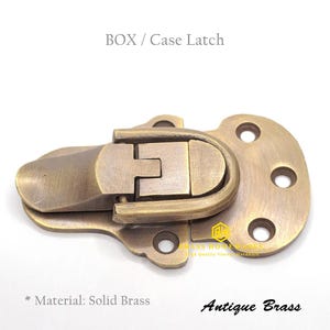 May include: Antique brass box or case latch with a spring-loaded mechanism. The latch is made of solid brass and has a rounded, oval-shaped handle. The latch is designed to be mounted on a box or case.