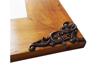 May include: A wooden picture frame with ornate metal corner accents. The frame is a light brown color and the metal accents are a dark brown color.