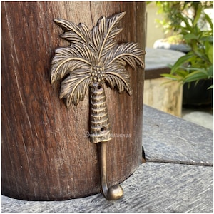 May include: A gold palm tree shaped hook. The hook is mounted on a wooden surface.