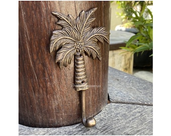 Puede incluir: Un gancho dorado con forma de palmera. El gancho está montado en una superficie de madera.