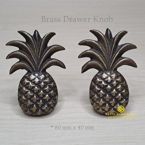 May include: Two gold pineapple drawer knobs, each measuring 60 mm by 40 mm. The knobs feature a detailed pineapple design with a textured surface.