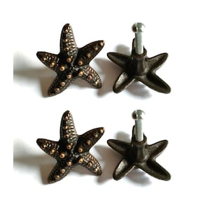 Op de afbeelding: Set van vier zwarte gietijzeren zeesterren-ladegrepen met een zilveren schroef. De zeesterren hebben een reliëf, textuurontwerp en een bronzen afwerking.