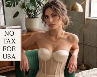 Puede incluir: Un corsé color crema con paneles transparentes y ballenas, combinado con pantalones a juego. La imagen muestra a una mujer sentada en una silla verde, sosteniendo gafas de sol. El texto "NO TAX FOR USA" es visible.