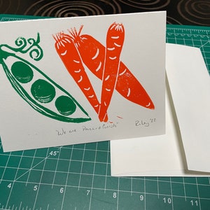 May include: A white card with a green pea pod and two orange carrots printed on it. The card has the text "We are Pousand Purrats" and "Riley '22" written on it.