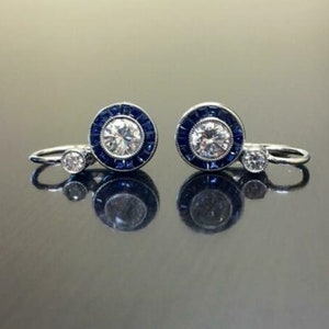 May include: A pair of silver earrings featuring a round, clear stone encircled by a halo of blue stones. Each earring has a smaller, clear stone dangling from the bottom.