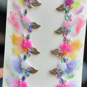 May include: A collection of eight colorful butterfly hair clips. Each clip features iridescent wings, a central flower, faux pearls, and decorative jewels. The wings display a gradient of colors, including pink, yellow, purple, and green, with a bronze leaf accent.