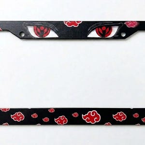 May include: A rectangular black license plate frame featuring a repeating pattern of red clouds with white outlines. The top section of the frame displays two stylized red eyes with black pupils and intricate iris details centered above the opening.