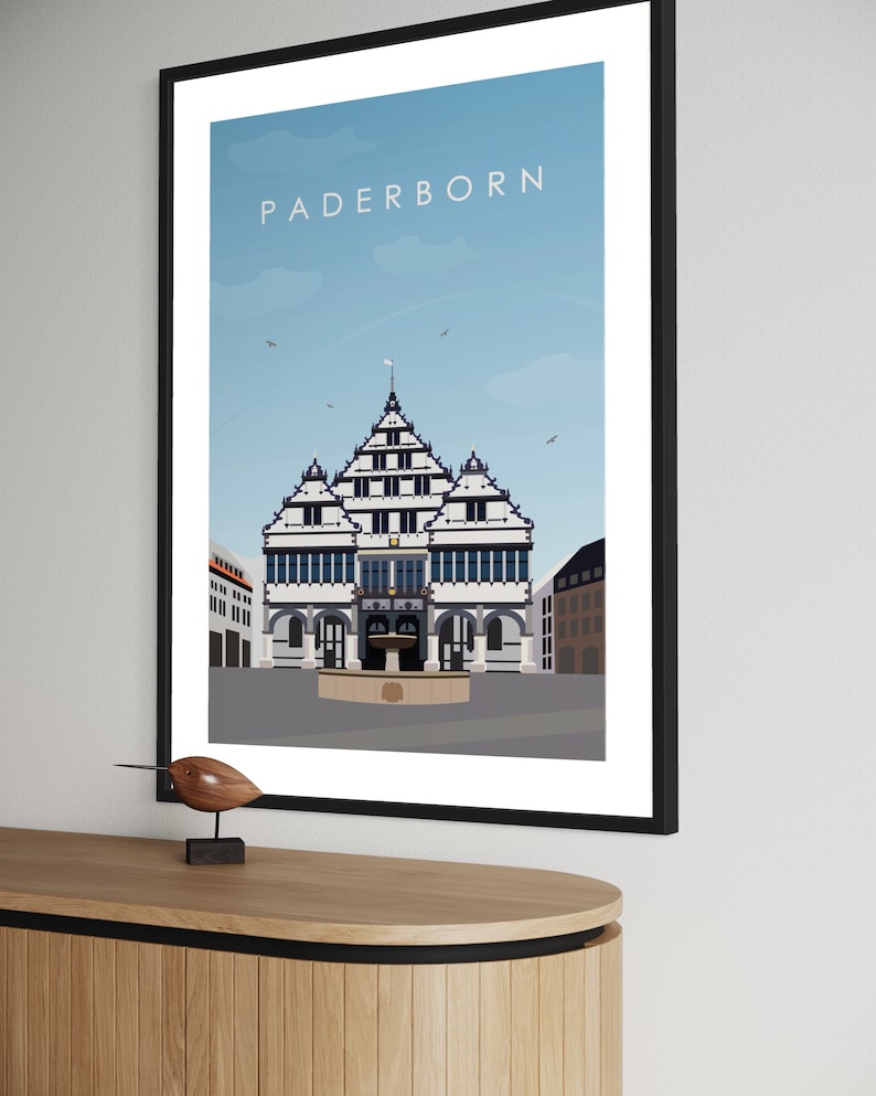 K&ouml;nnte beinhalten: Eine farbenfrohe Illustration des Rathauses in Paderborn, Deutschland. Das Geb&auml;ude ist wei&szlig; mit schwarzen Verzierungen und einem blauen Dach. Der Himmel ist blau mit wei&szlig;en Wolken. Der Text "Paderborn" ist in wei&szlig;en Buchstaben oben im Bild geschrieben.