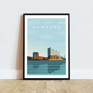 Op de afbeelding: Een zwart ingelijste poster met een minimalistische illustratie van de skyline van Hamburg. De poster toont de Elbphilharmonie en andere gebouwen in de stad. De tekst "HAMBURG" is in wit bovenaan de poster gedrukt.