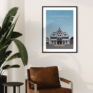 K&ouml;nnte beinhalten: Ein schwarzer gerahmter Druck mit blauem Himmel und wei&szlig;en Wolken. Der Druck zeigt eine Schwarzwei&szlig;illustration eines Geb&auml;udes mit dem Text "Paderborn" oben.