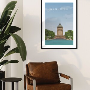 K&ouml;nnte beinhalten: Eine gerahmte Illustration eines Geb&auml;udes mit einem Turm vor einem Gew&auml;sser. Der Text "MANNHEIM" befindet sich oben auf der Illustration.