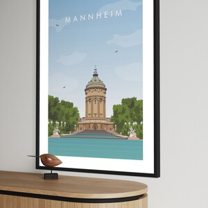 K&ouml;nnte beinhalten: Ein minimalistisches Poster mit blauem Himmel und wei&szlig;en Wolken. Das Poster zeigt ein braunes Geb&auml;ude mit gr&uuml;nem Dach und dem Wort "MANNHEIM" in schwarzer Schrift oben.
