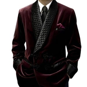 May include: A burgundy velvet blazer with a black quilted shawl collar and a black tie. The blazer has a double-breasted closure with decorative buttons.