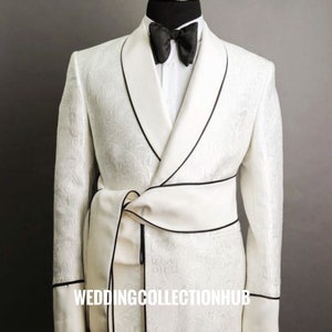 May include: A white tuxedo jacket with a black satin lapel and a black bow tie. The jacket has a white satin sash with a black trim and the text "WEDDINGCOLLECTIONHUB" is printed on the sash.
