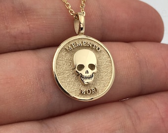 May include: Gold necklace with a round pendant featuring a skull and the words "Memento Mori".
