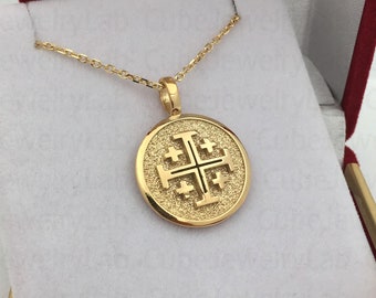 May include: A gold necklace with a round pendant featuring a cross with four smaller crosses. The pendant is textured and has a shiny finish. The necklace is in a red velvet box with the words "Gold Cube Jewelry Lab" printed on the lid.