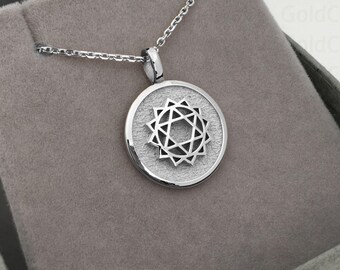 May include: A silver pendant necklace featuring a circular pendant with a geometric star design. The necklace is displayed in a gray jewelry box with a velvet lining. The pendant hangs from a delicate chain.