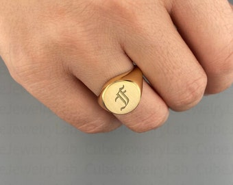 May include: A gold signet ring with a raised oval top featuring the letter "F" in a gothic font.