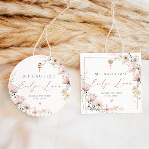 May include: Two white favour tags with floral designs and the text "MI BAUTIZO Evelyn Luna GRACIAS POR VENIR 9 DE JUNIO". One tag is round and the other is square.