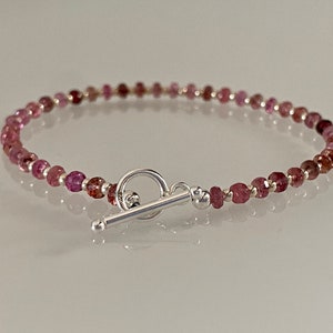 Op de afbeelding: Een delicate armband gemaakt met kleine roze en rode edelsteen kralen en een zilveren toggle sluiting.