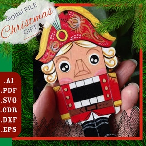 Puede incluir: Un adorno de madera de cascanueces pintado en rojo, amarillo y blanco con una boca y ojos negros. El adorno está siendo sostenido por una mano. El texto "digital FILE Christmas GIFT" está en la esquina superior izquierda de la imagen.