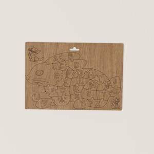 K&ouml;nnte beinhalten: Holzpuzzle in Form eines Fisches mit einer Katze und einem Hund an beiden Enden. Die Puzzleteile sind mit den Buchstaben A bis Z beschriftet.