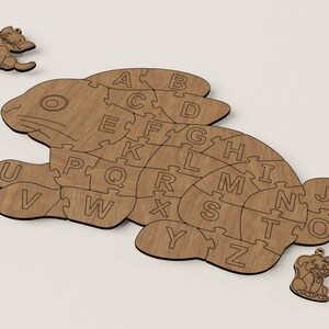 K&ouml;nnte beinhalten: Holzpuzzle eines Kaninchens, wobei jedes St&uuml;ck die Form eines Buchstabens des Alphabets hat. Das Puzzle ist aus hellbraunem Holz gefertigt und hat eine nat&uuml;rliche Holzoptik.