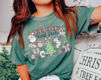 Puede incluir: Una camiseta verde con un diseño navideño que incluye el texto "HOLLY JOLLY Rad Tech". El diseño incluye un árbol de Navidad, bastones de caramelo, un gorro de Papá Noel, una taza de chocolate caliente y una bola de nieve.