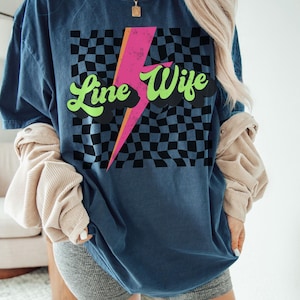 May include: A blue t-shirt with a checkered pattern, a pink lightning bolt, and the text "Line Wife" in green and white lettering.
