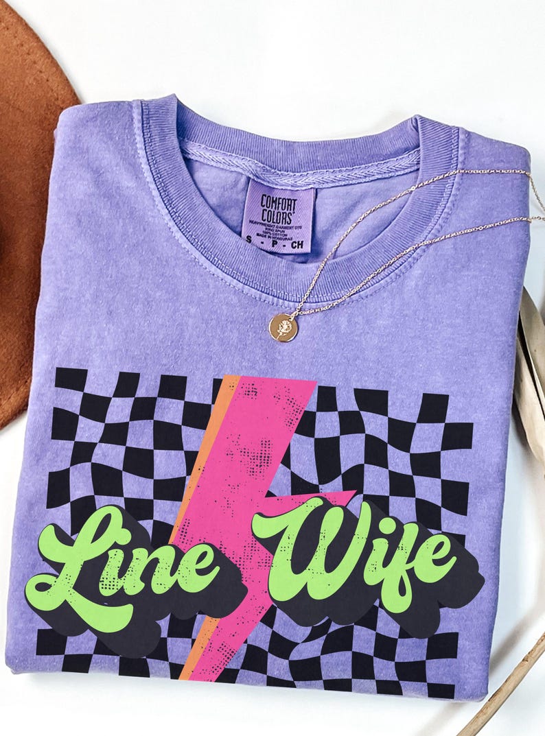 May include: Purple t-shirt with a black and white checkered pattern, a pink lightning bolt, and the text "Line Wife" in green.