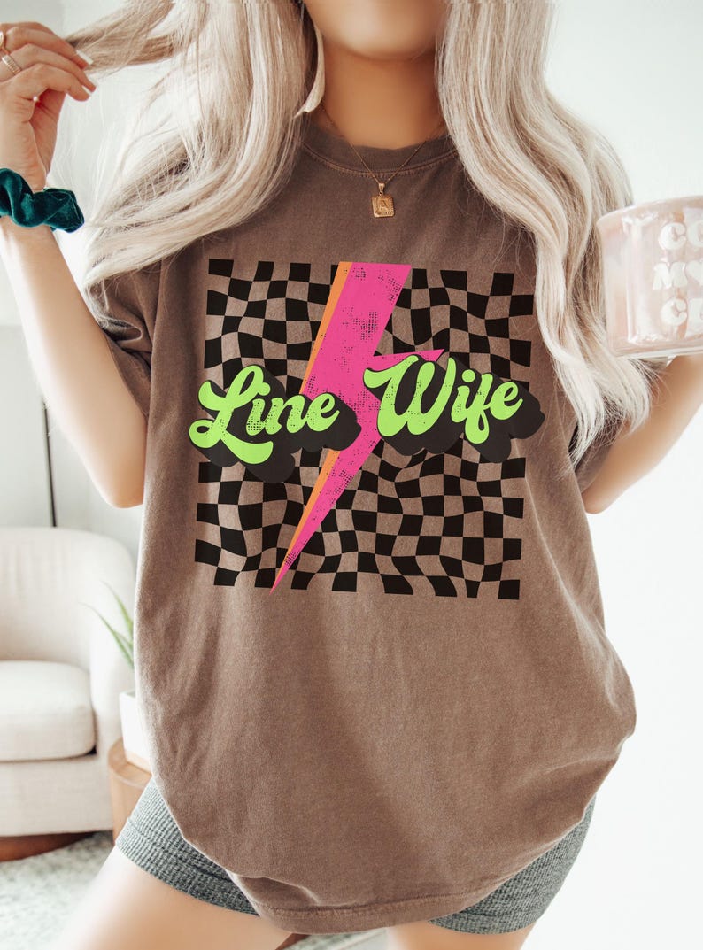 May include: A brown t-shirt with a black and white checkered pattern, a pink lightning bolt, and the text "Line Wife" in green.