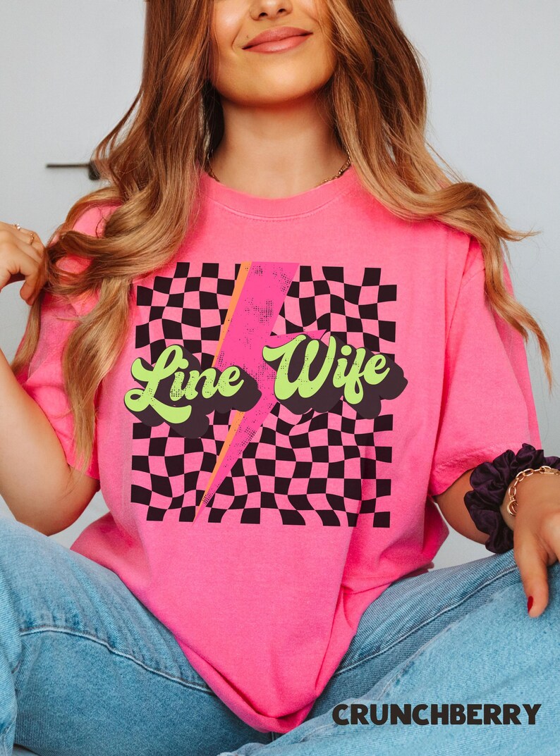May include: Pink t-shirt with a black and white checkered pattern, a lightning bolt, and the text "Line Wife" in a retro font.