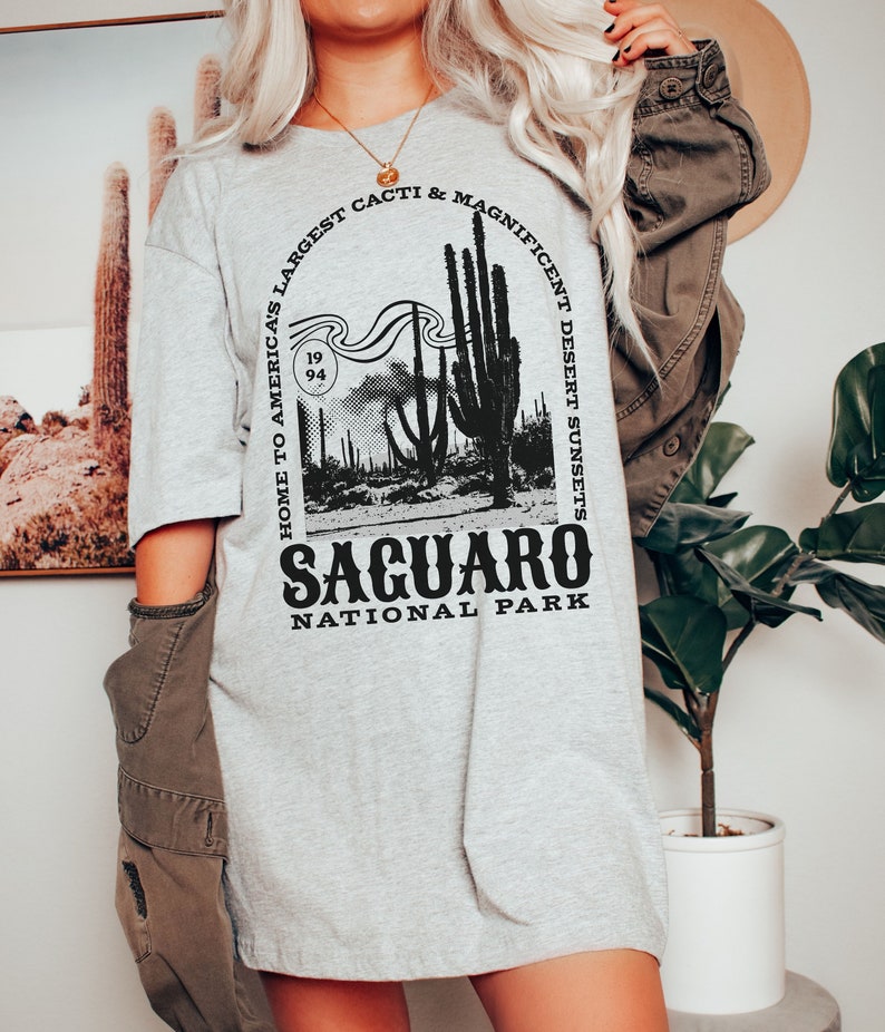 May include: A gray t-shirt with a black graphic design featuring a Saguaro cactus and the text "Home to America's Largest Cacti & Magnificent Desert Sunsets, Saguaro National Park".