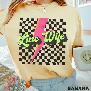 May include: A yellow t-shirt with a black and white checkered pattern, a pink lightning bolt, and the text "Line Wife" in green and yellow letters.