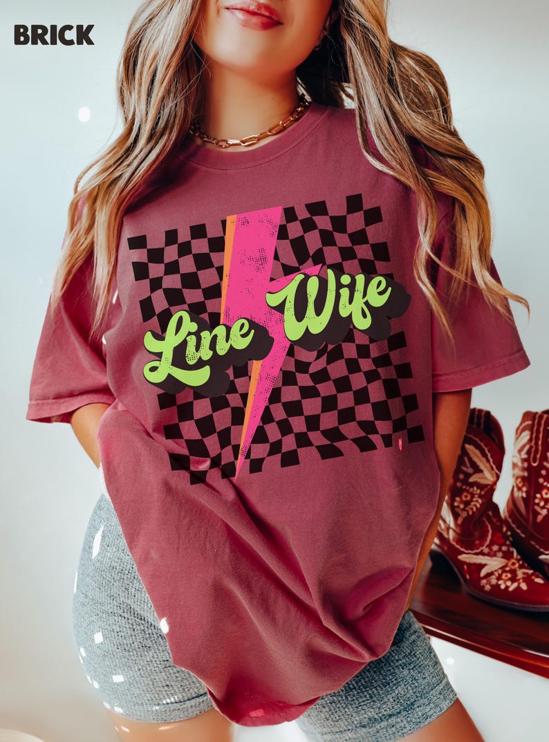 May include: A brick red t-shirt with a black and white checkered pattern, a pink lightning bolt, and the text "Line Wife" in green and black.