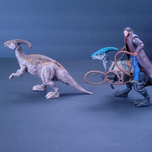 Pu&ograve; includere: Due giocattoli di dinosauro, uno marrone e uno blu, con una action figure da cowboy che cavalca il dinosauro blu.