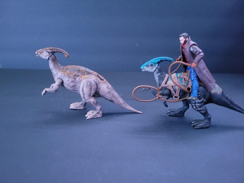Pu&ograve; includere: Due giocattoli di dinosauro, uno marrone e uno blu, con una action figure da cowboy che cavalca il dinosauro blu.