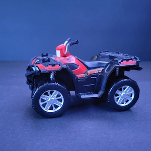 May include: A toy ATV in black and red with silver wheels. The ATV has a red roll cage and a black body. The wheels have a silver star design. The ATV is a miniature replica of a real ATV.