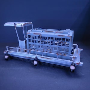 Peut inclure: Un modèle gris d'un petit bateau avec une cage sur le pont. Le bateau a une petite cabine avec un toit et une rambarde autour du périmètre. Il y a quatre petites lumières suspendues au fond du bateau.