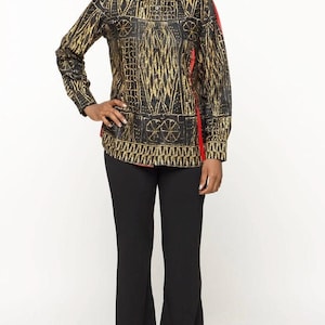 Puede incluir: Una camisa abotonada de manga larga con un estampado geométrico negro y dorado, combinada con pantalones negros acampanados. La camisa tiene un acento rojo en el lateral. El atuendo es adecuado para diversas ocasiones.