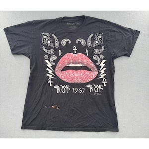 May include: A black short-sleeve t-shirt featuring a large pink paisley-patterned lip graphic in the center. The design includes white paisley accents, lightning bolts, ankh symbols, and the text ROF 1967 ROF printed in a stylized font.