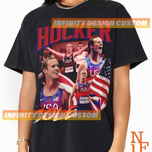 May include: Black t-shirt with a vintage-style graphic of a group of runners wearing USA uniforms. The graphic includes the text "HOLKER" and "INFINITY DESIGN CUSTOM".