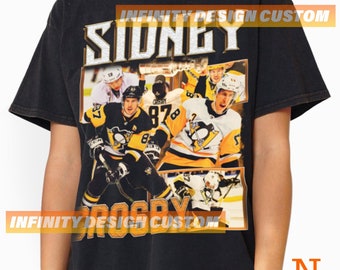 May include: Black t-shirt with a vintage-style graphic of Sidney Crosby and the Pittsburgh Penguins hockey team. The graphic includes the text "Sidney" and "Crosby" and the team's logo. The shirt also features the text "Infinity Design Custom".