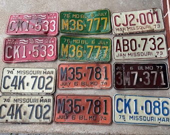 May include: A collection of vintage Missouri license plates in various colors, including red, green, orange, and blue. The plates display different numbers and letters, with years ranging from the 1970s. Some plates show signs of wear and tear.