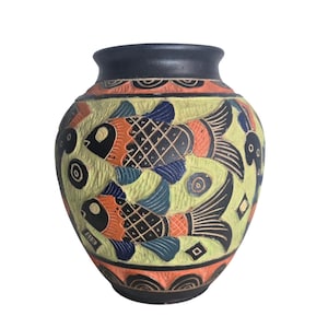 May include: A ceramic vase with a matte black rim and base, featuring a textured light green background decorated with orange and black fish motifs. The surface displays intricate carved patterns, including geometric shapes and wave-like designs.