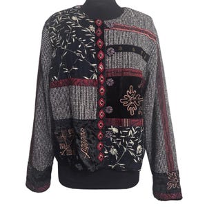 May include: A long-sleeved jacket featuring a patchwork design with black, white, and deep red panels. The garment includes textured fabric sections, floral patterns, and embroidered geometric details along the front button closure.