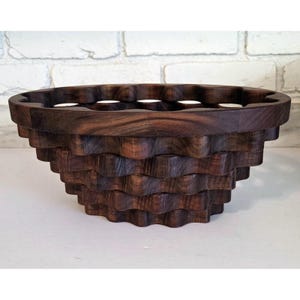 May include: A handcrafted, dark brown wooden bowl with a unique, layered design. The bowl's exterior features a wave-like pattern, and the top rim has evenly spaced circular cutouts. The bowl is likely used for decorative or functional purposes.