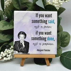 Könnte beinhalten: Eine quadratische Keramikfliese mit einem schwarz-weißen Porträt von Margaret Thatcher und dem Zitat: If you want something said, ask a man; if you want something done, ask a woman. Der Hintergrund ist ein hellvioletter Aquarellverlauf.