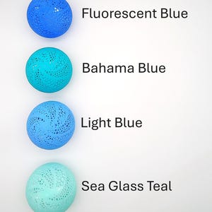 May include: Four round, crocheted, decorative balls in shades of blue and teal. The balls are arranged vertically from top to bottom. The colors are labeled as Fluorescent Blue, Bahama Blue, Light Blue, and Sea Glass Teal.